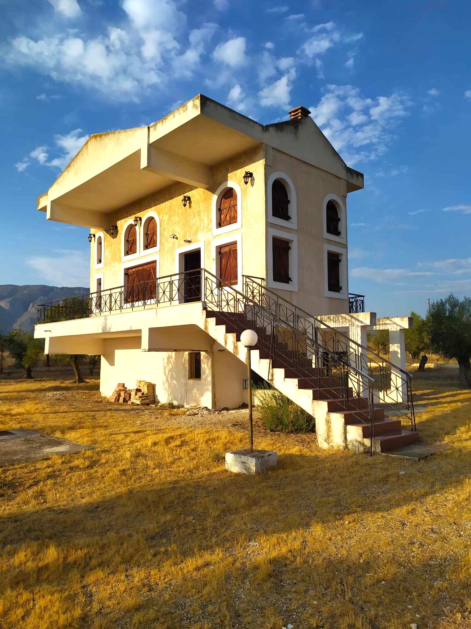 The estate house at golden hour, with wide terraces and arched shuttered windows